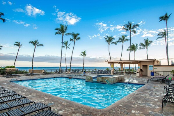 A swimming pool with lounge chairs, palm trees, and a view of the ocean.