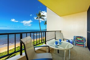 A balcony with a view of the beach, a table with chairs, and a colorful beach chair. - Gorgeous Oceanfront Retreat! Marvel at the Stunning Views from Sugar Beach #326 (Kihei, Maui)