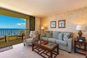 A hotel room with a balcony, a sofa, armchairs, a coffee table, and a lamp.