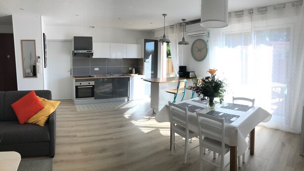 A modern living room with a sofa, a dining table with chairs, and a kitchen in the background. - LE Logis DES Jalles (Saint-Médard-en-Jalles)