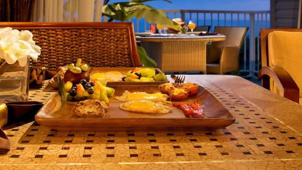 Un plateau de petit-déjeuner avec divers aliments, une chaise en osier et une vue sur l’océan.