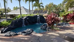 Un espace piscine agrémenté d’une cascade, entouré de plantes tropicales et de palmiers.