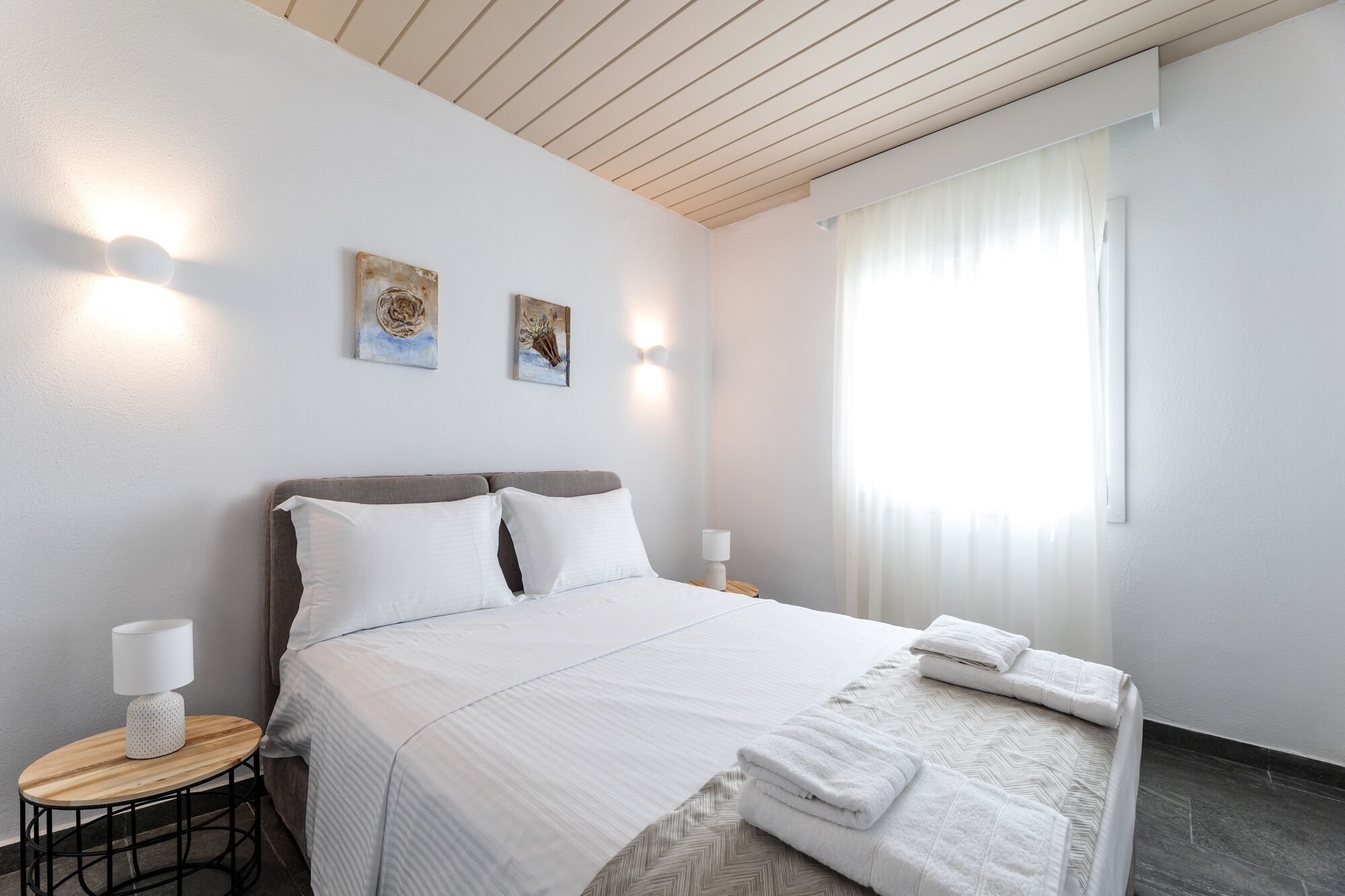 A modern hotel room with a large bed, two bedside tables, and artwork on the wall.