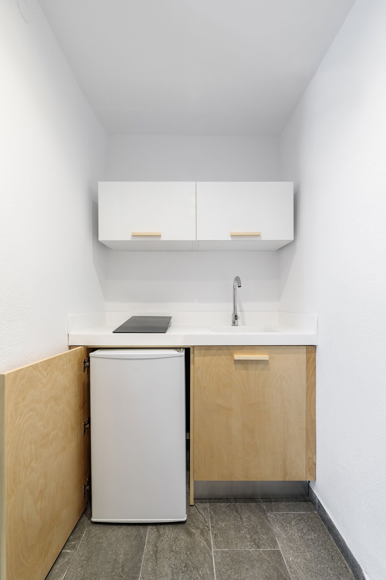 Una cocina compacta con encimera blanca, un lavabo y un refrigerador blanco pequeño.