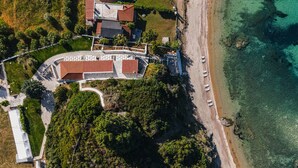 Vista aérea de una propiedad costera con playa, piscina y un edificio de techo rojo.