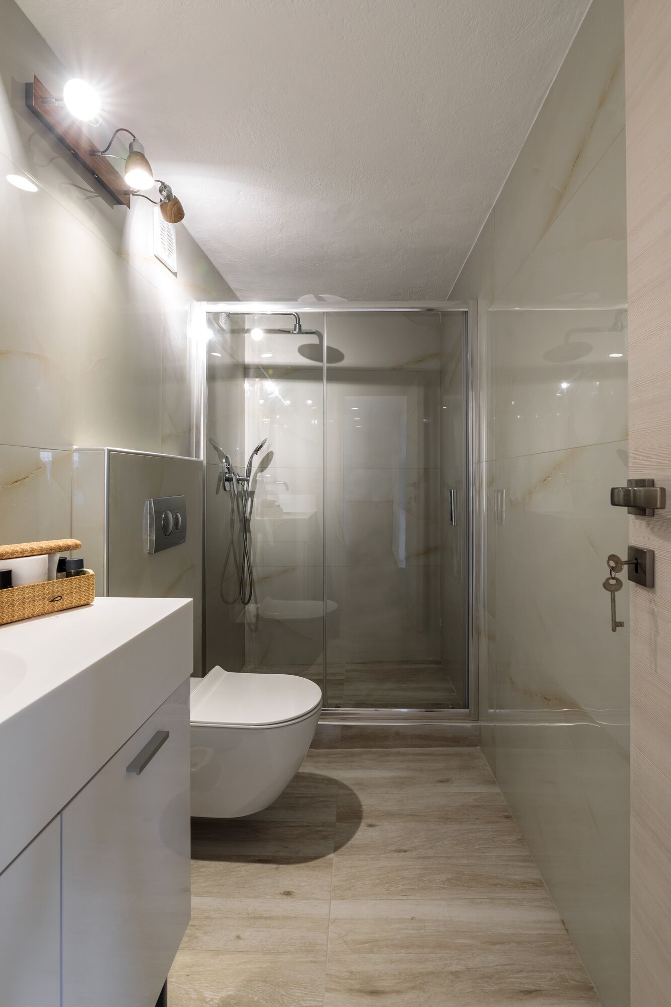 Une salle de bain moderne avec une douche à parois de verre, des toilettes blanches et un meuble-lavabo agrémenté d’un panier contenant des articles de toilette.