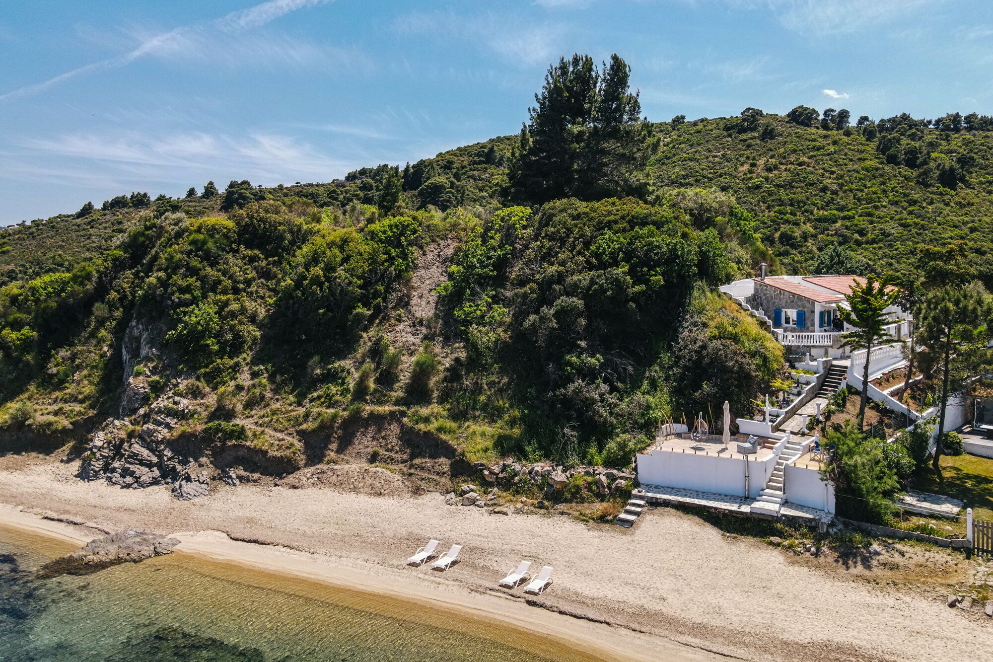 A coastal property with a beach, a staircase leading to a house, and a rocky hillside.