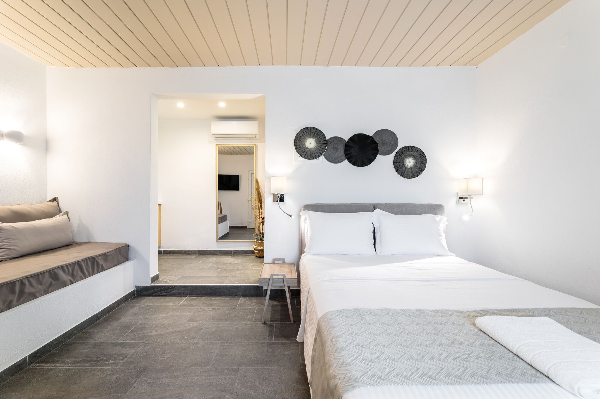 A modern hotel room with a bed, a seating area, and a view into the bathroom.