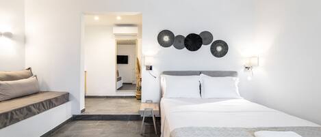 A modern hotel room with a bed, a seating area, and a view into the bathroom.