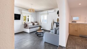 Una sala de estar moderna con sofá, una mesa de centro y chimenea. Hay un televisor montado en la pared y una ventana con vistas al exterior.