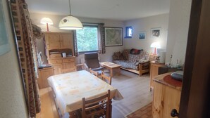 Uma sala de estar aconchegante com sofá, mesa de jantar e armários de madeira. Há duas luminárias sobre a mesa e uma janela com cortinas.