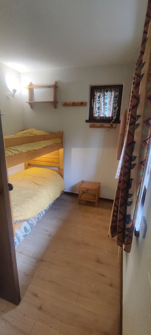 Een kleine, knusse kamer met een stapelbed, een klein houten tafeltje en een raam met gordijnen.