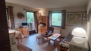 Quarto aconchegante com uma escrivaninha de madeira, uma cadeira, um sofá e uma televisão. Há janelas com cortinas, um mapa na parede e um abajur.