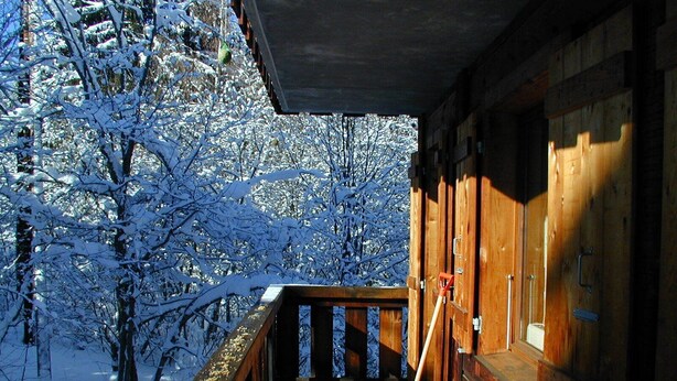 Uma cabana de madeira com varanda dando para uma floresta coberta de neve.