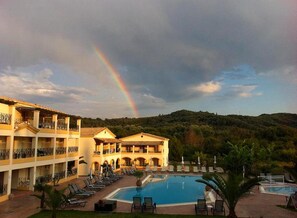 A hotel with a pool, multiple balconies, and a view of a hilly landscape. - Corfu Village Studios (Corfu)