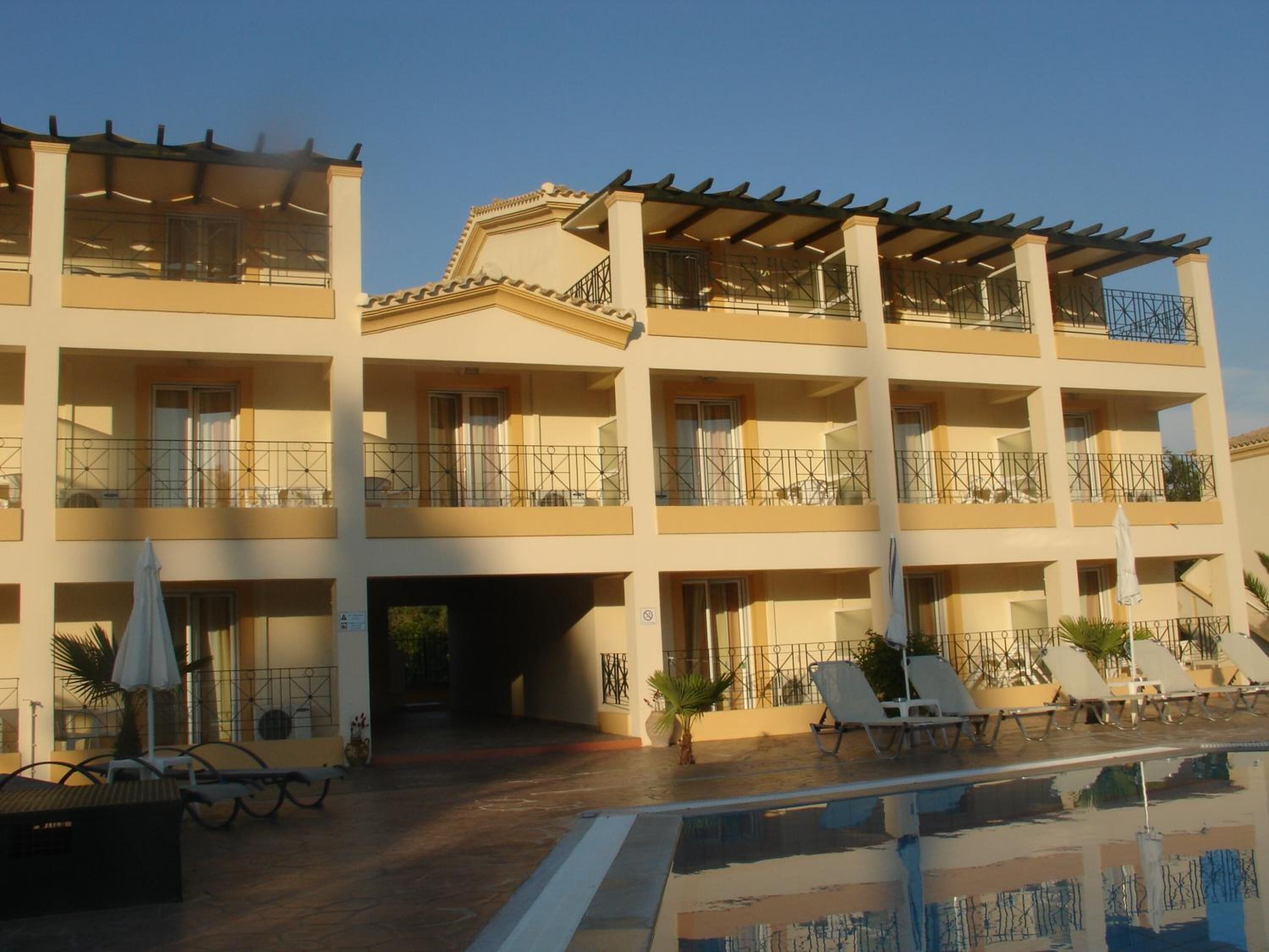 Un hotel de varios pisos con balcones, piscina y mobiliario exterior.