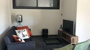 Ein modernes Wohnzimmer mit einem grauen Sofa, einem grünen Sessel, einem schwarzen Couchtisch, einem Fernseher auf einem Holzboden und einer schwarzen Vase.