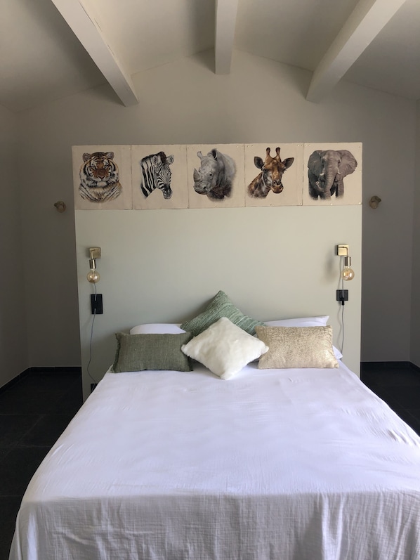 A bedroom with a bed, pillows, and a wall-mounted artwork of animal heads.