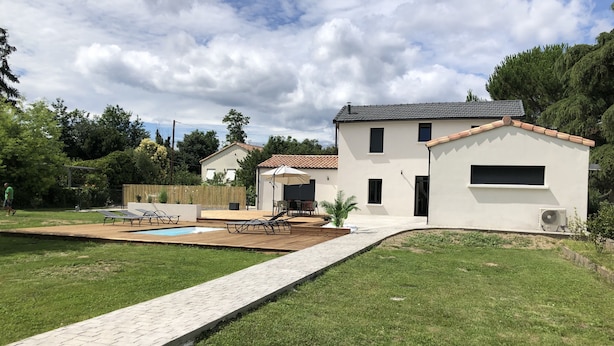 Ein modernes Haus mit Swimmingpool, einer Terrasse mit Liegestühlen und einem gepflegten Rasen.
