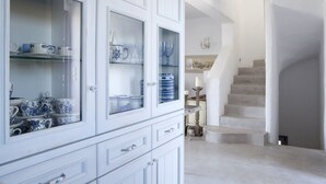 A white cabinet with glass doors displaying blue and white ceramic items. A staircase leads to a landing with a decorative candle and a small statue. - EXECUTIVE VILLA WITH PRIVATE SWIMMING POOL (PAROS)