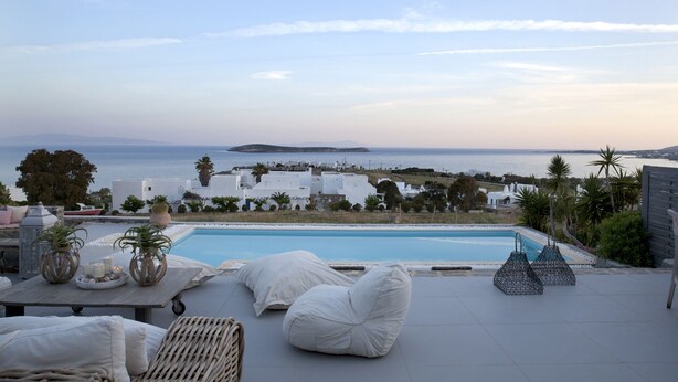 A poolside area with a view of the sea and white buildings in the background. - EXECUTIVE VILLA WITH PRIVATE SWIMMING POOL (PAROS)