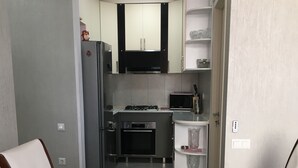 A modern kitchen with a refrigerator, microwave, stove, and oven. There is a dining table with chairs and a bowl of fruit. - Уютная квартира в Батуми с джакузи. (Batumi)