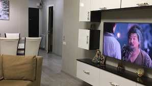 A modern living room with a flat-screen TV mounted on a white cabinet, a beige sofa, and a small coffee table with a decorative bowl. - Уютная квартира в Батуми с джакузи. (Batumi)