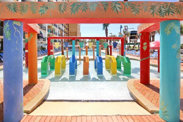 A water play area with colorful structures and a pool in the background.
