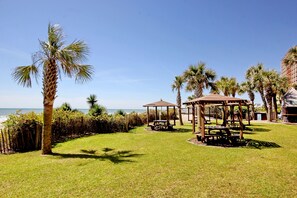 A grassy area with a wooden gazebo and palm trees, overlooking a body of water.