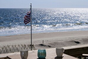A beach view with a flag, a wooden deck, and three cups. - Beach Please Oceanfront (Oak Island)