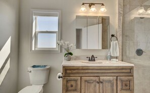 A bathroom with a toilet, a sink with a mirror, and a shower area. - Beach Please Oceanfront (Oak Island)