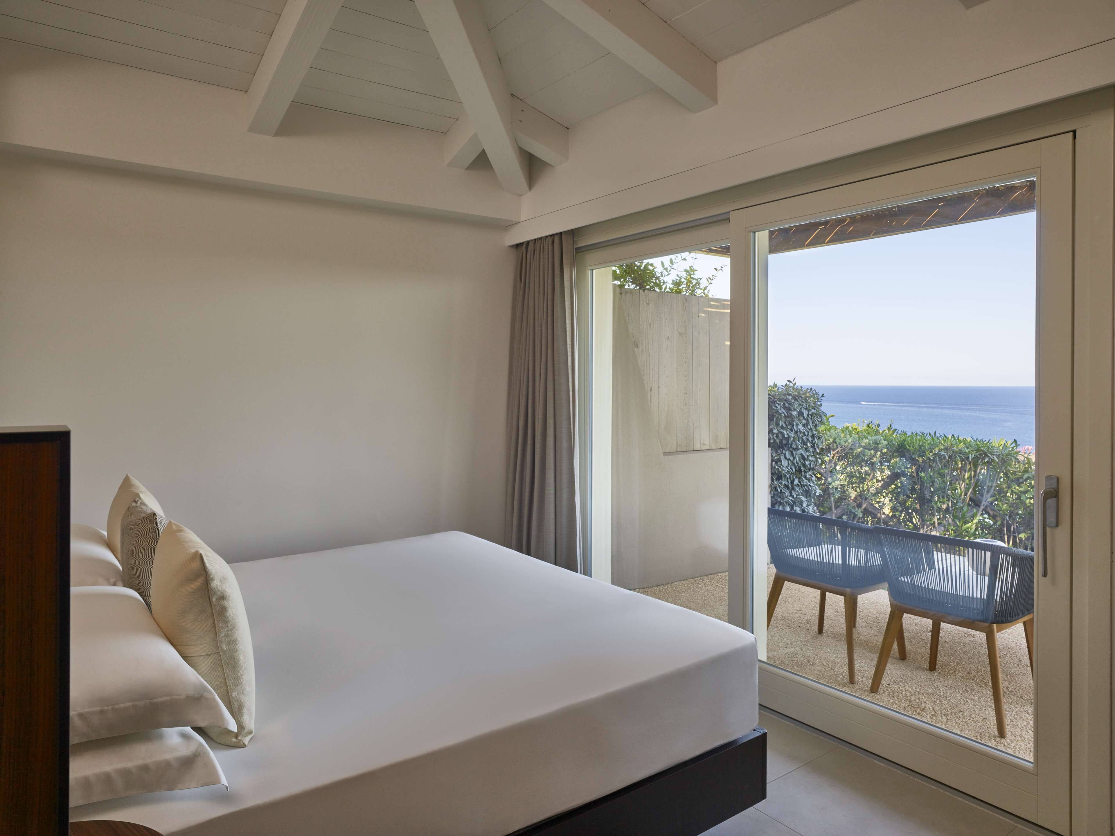 A bedroom with a bed, a view of the sea, and a balcony with chairs.