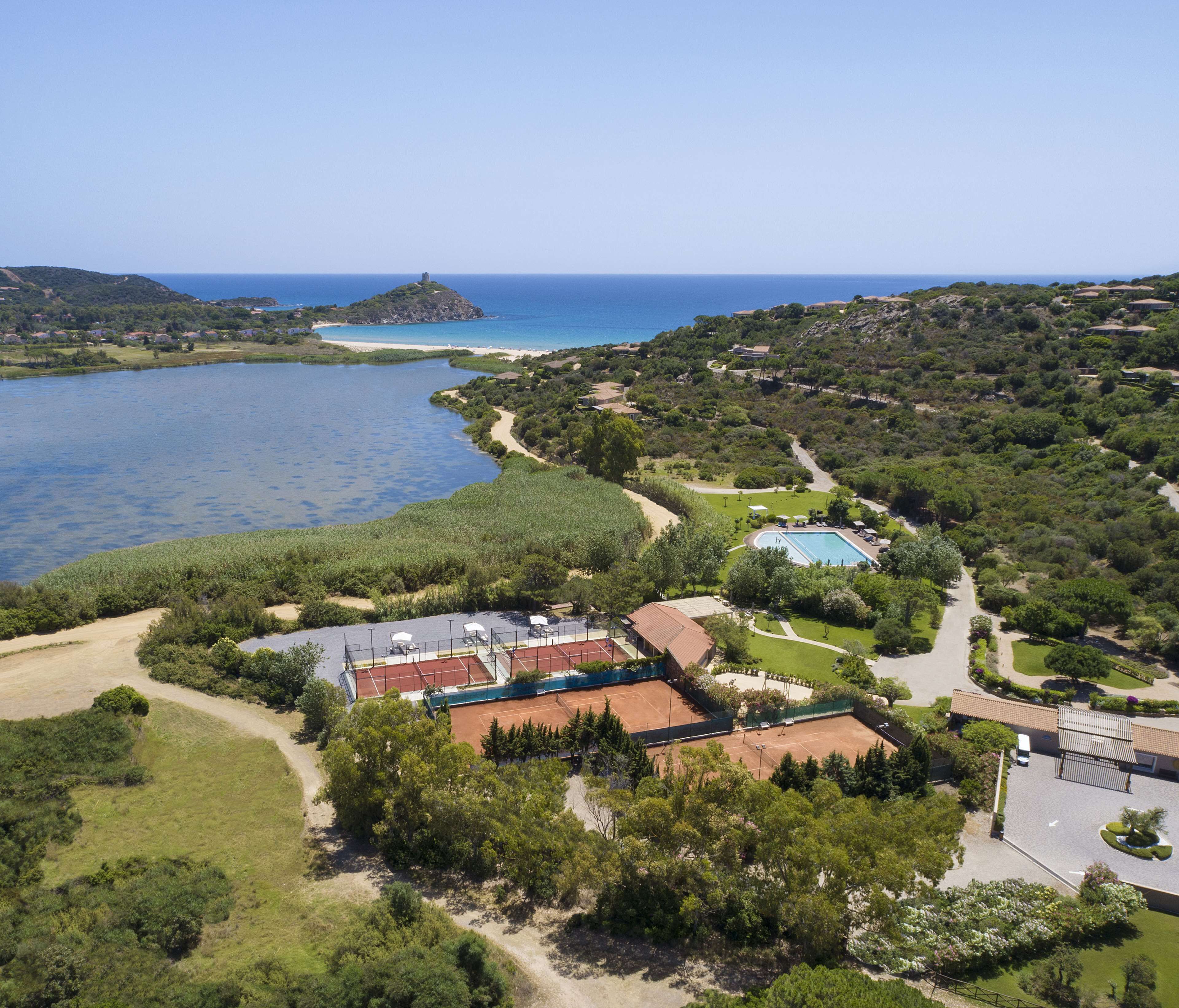 Ein Luftbild eines Küstenresorts mit Tennisplatz, Schwimmbad und Blick auf das Meer und die Hügel.