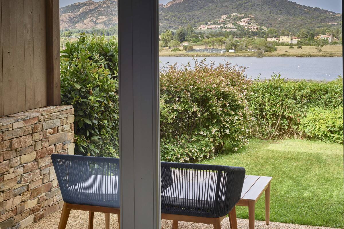 Eine Terrasse mit zwei Stühlen und einem Tisch, mit Blick auf einen See und Hügel.