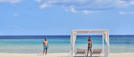 A beach with a wooden walkway leading to a white canopy with two chairs.