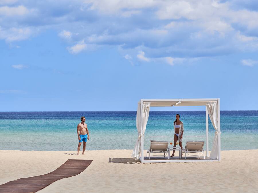 A beach with a wooden walkway leading to a white canopy with two chairs.