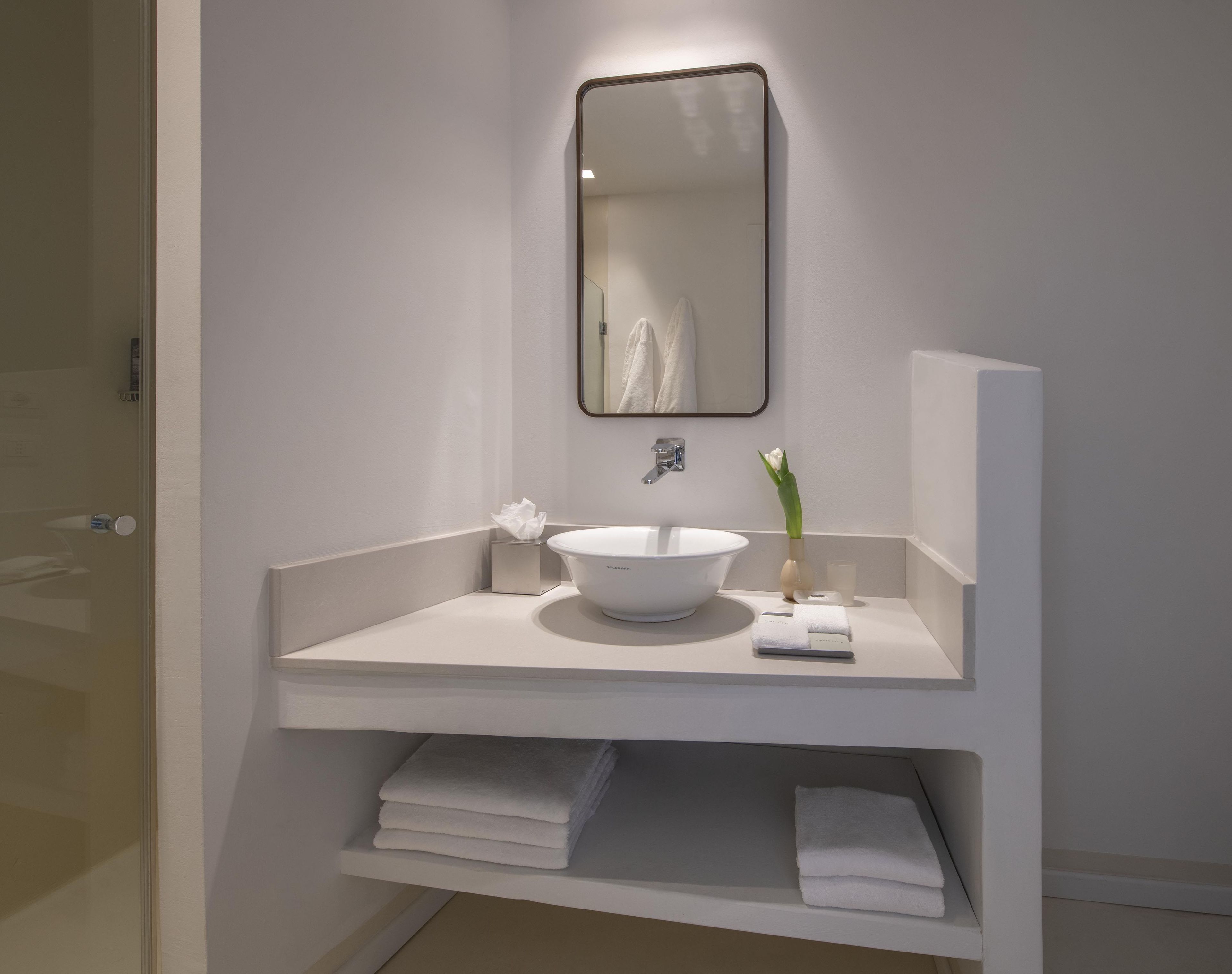 A modern bathroom with a white sink, mirror, and towel storage.