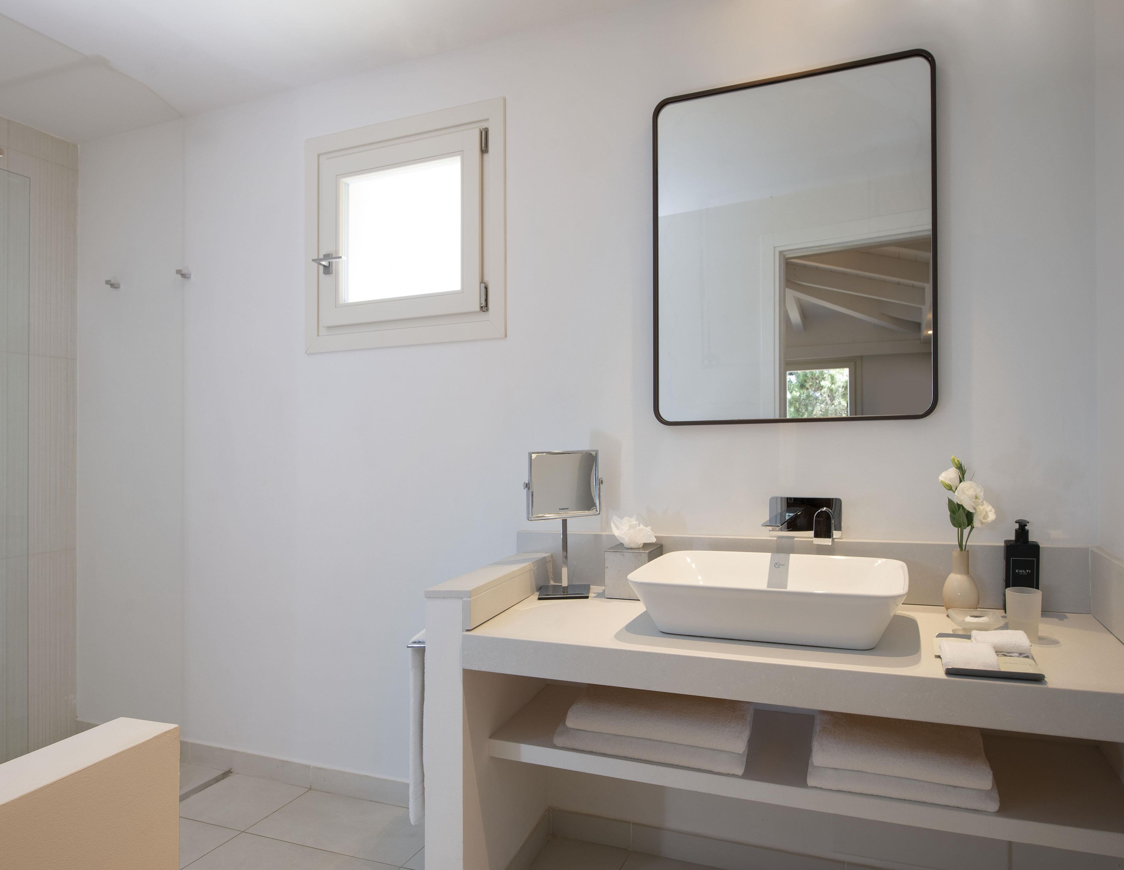 Un baño moderno con un espejo grande, un lavamanos blanco y una ventana pequeña.
