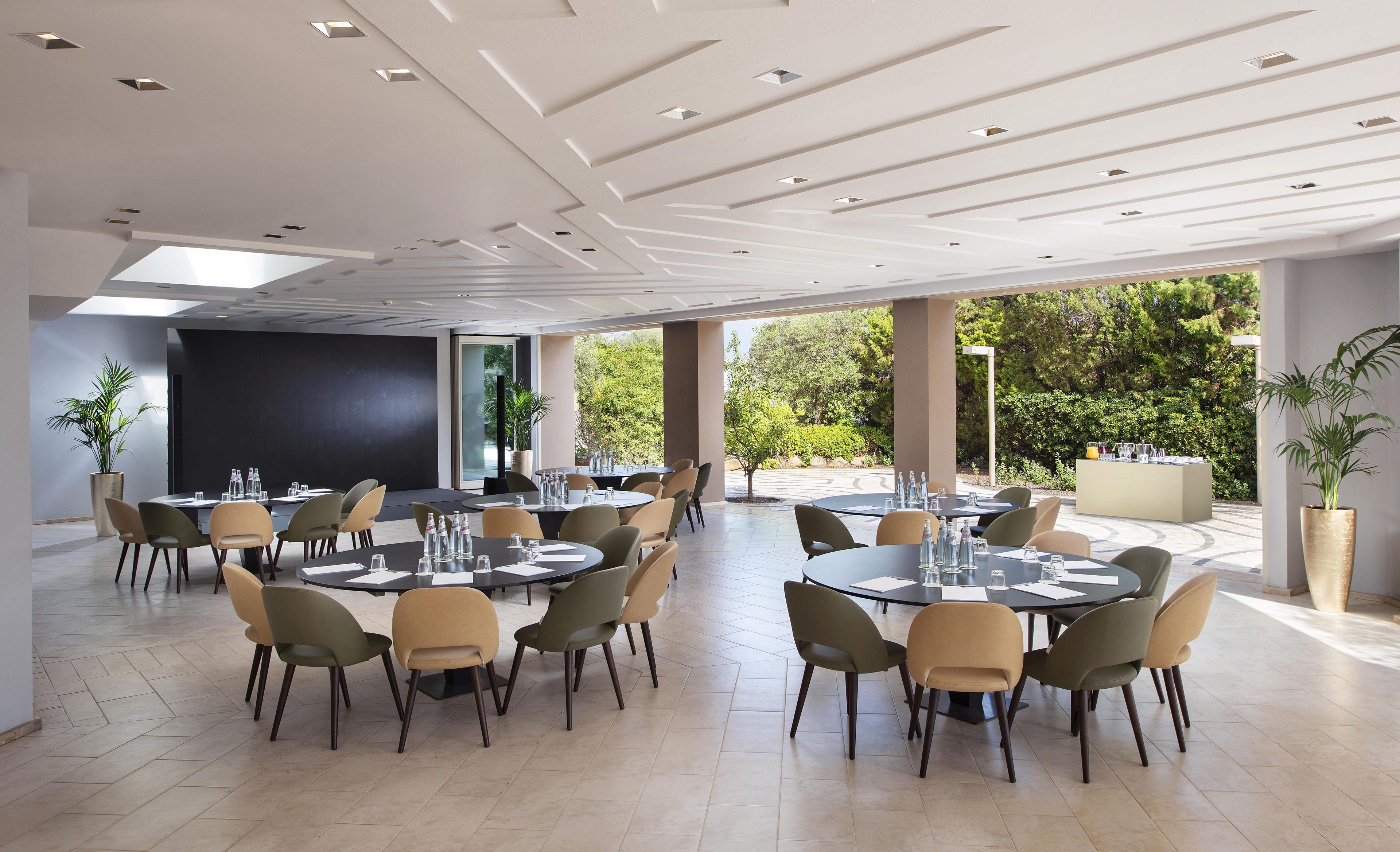 A spacious indoor dining area with round tables and chairs, large windows, and a modern ceiling design.