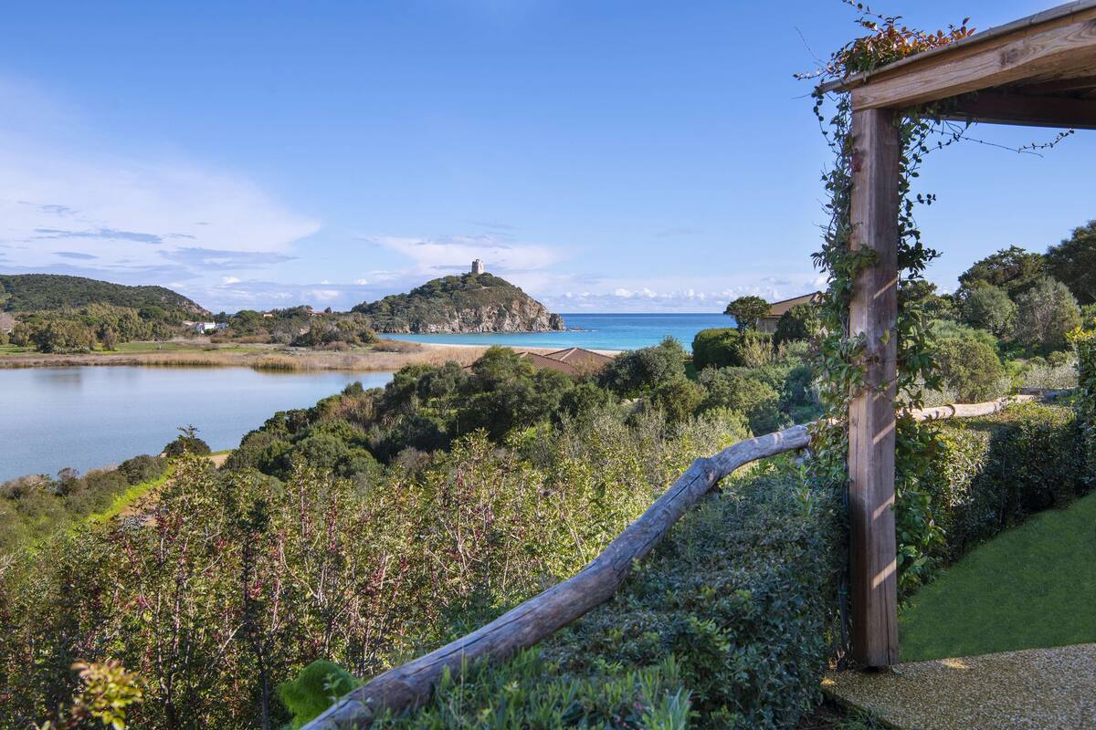 Eine Küstenlandschaft mit einer Holzpergola, üppigem Grün und einer fernen Insel mit einem Turm.
