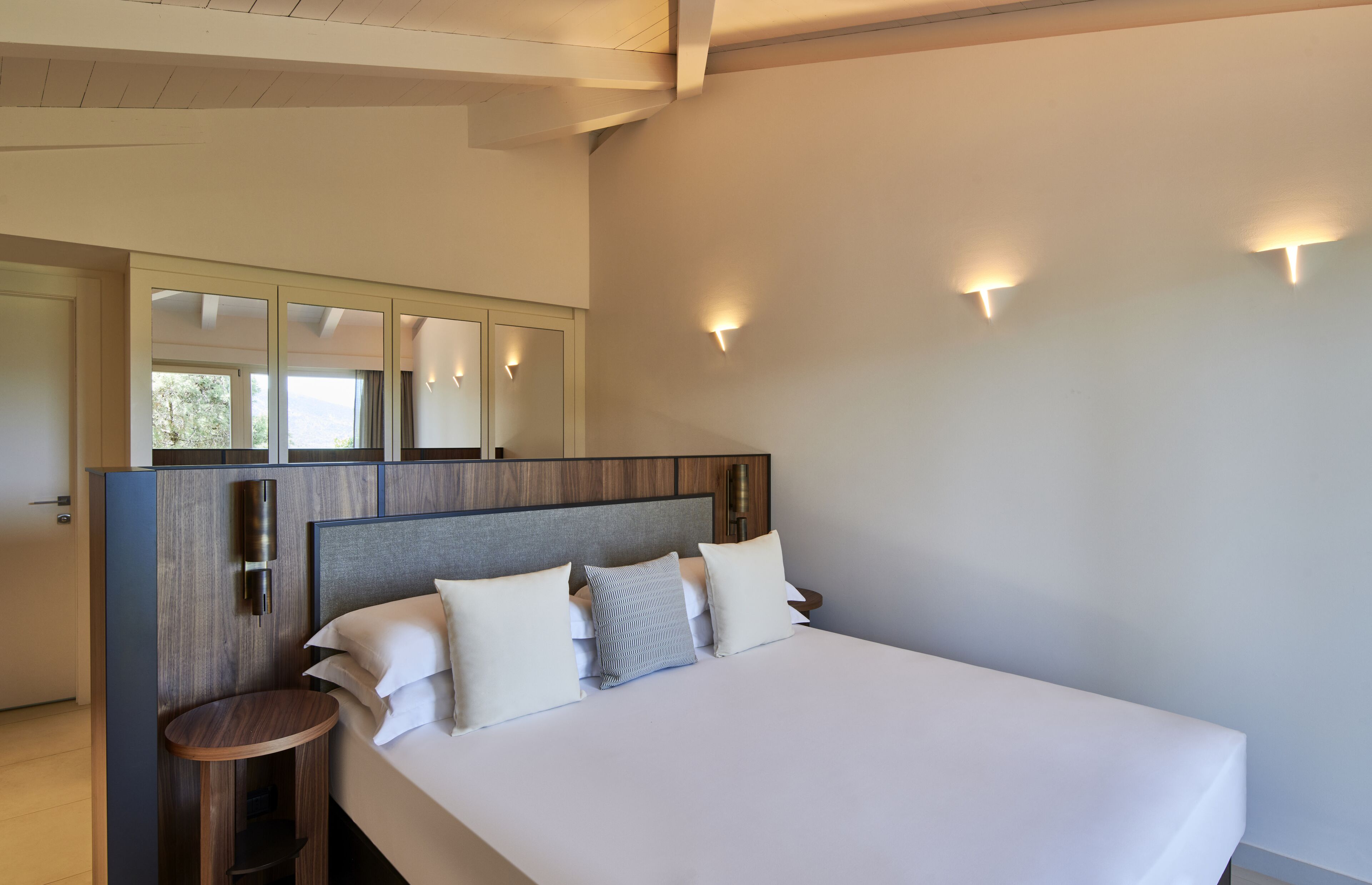 A modern hotel room with a large bed, a wooden headboard, and a small round table.