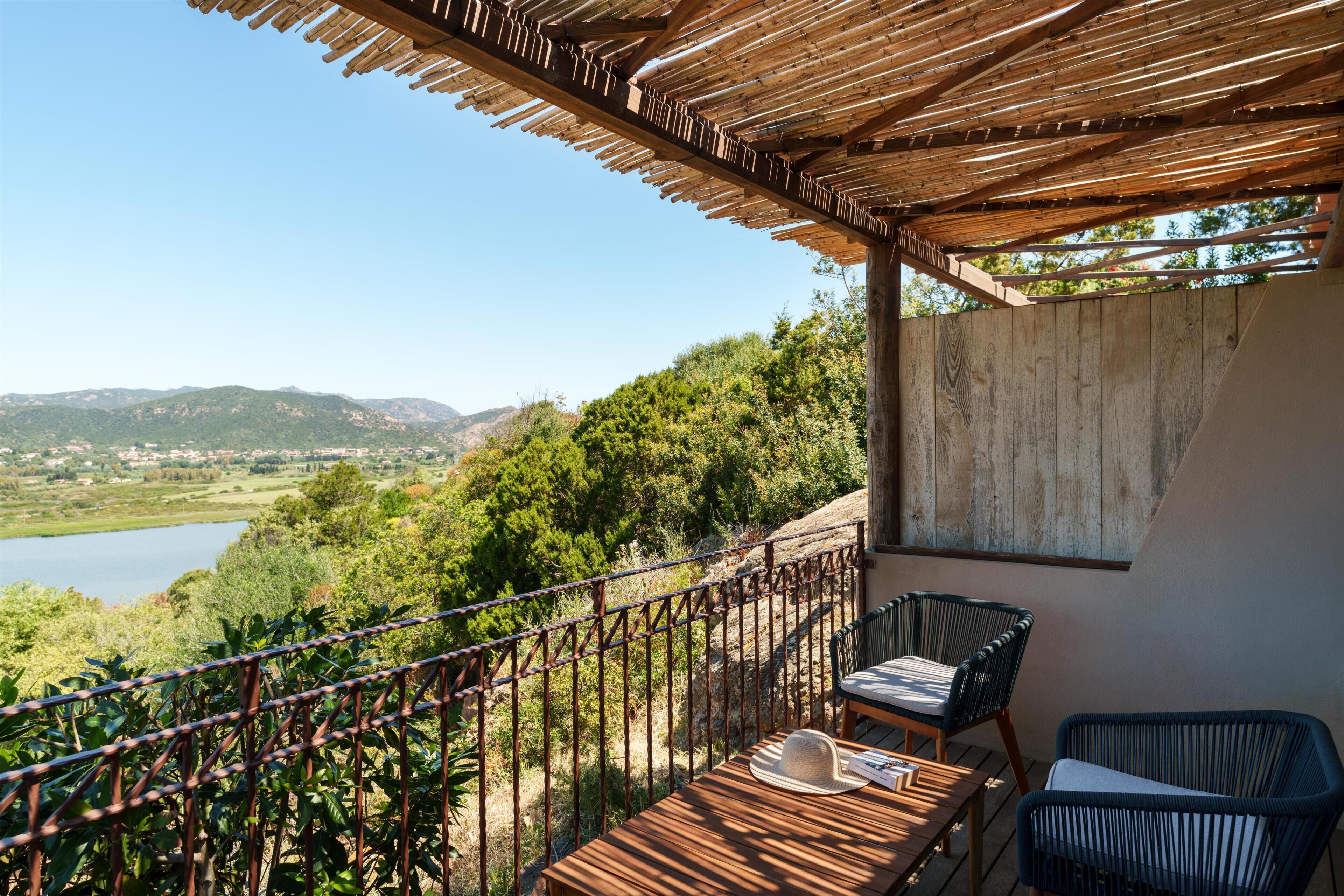 Ein Balkon mit Holztisch und -stühlen mit Blick auf einen See und Hügel.