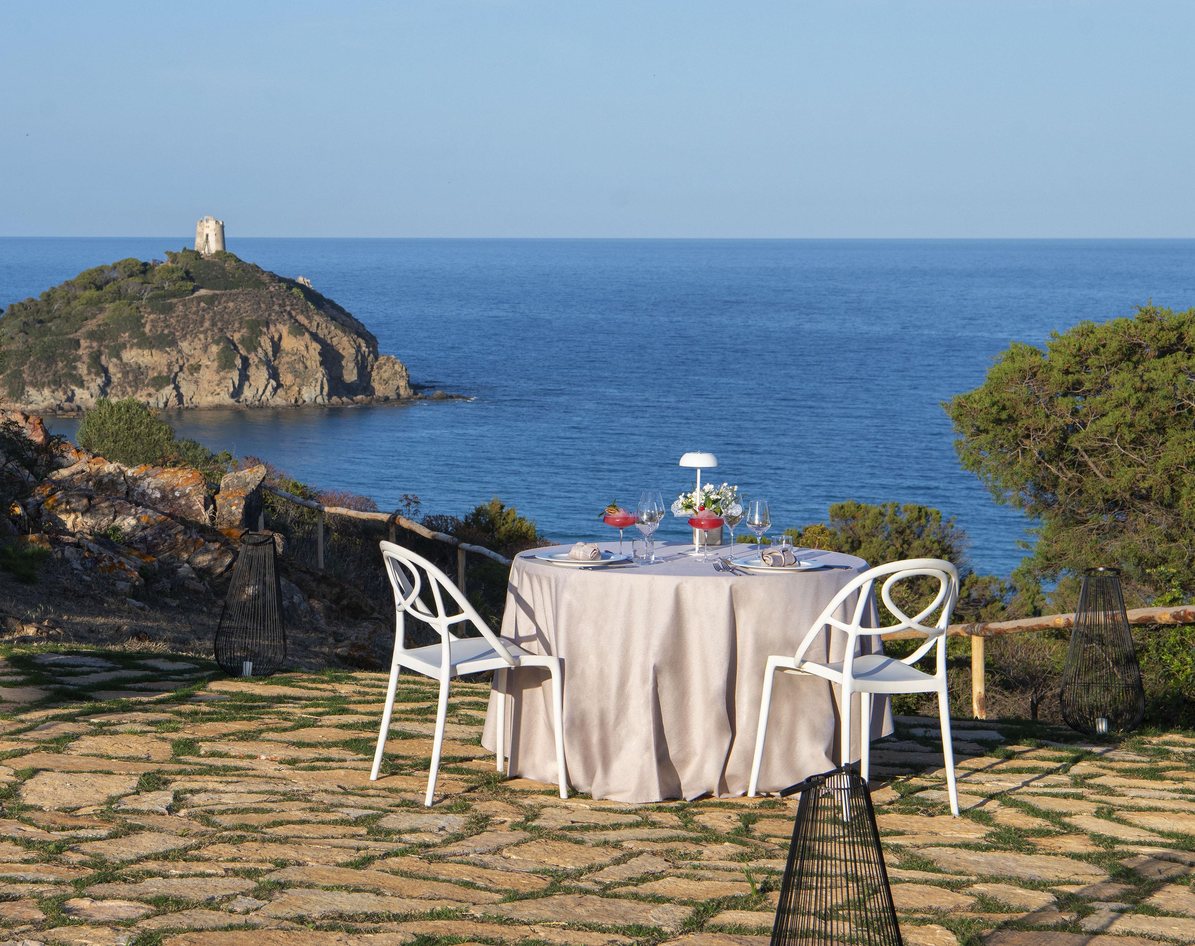 Une table dressée pour deux personnes, avec vue sur la mer et un phare en arrière-plan.