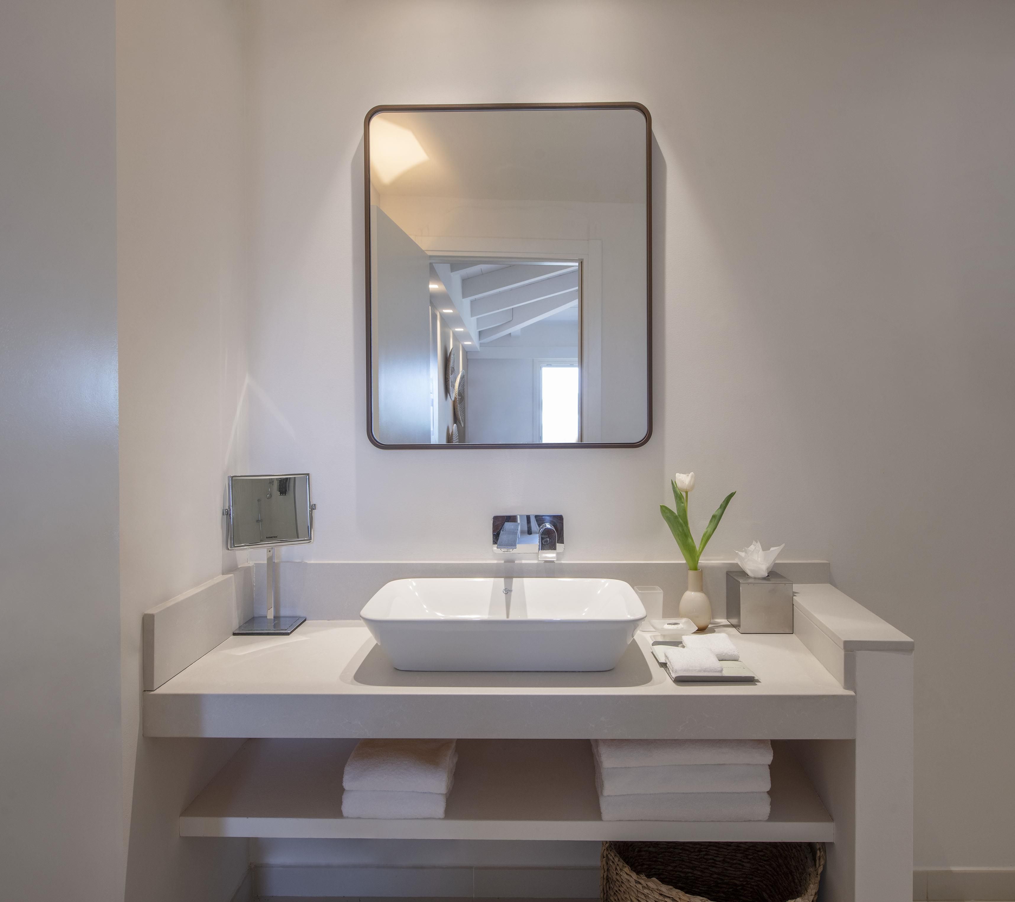 A modern bathroom with a white vanity, a large mirror, and a built-in shelf for towels.