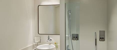 Un baño moderno con un lavabo redondo, ducha con mampara de vidrio y un espejo grande.