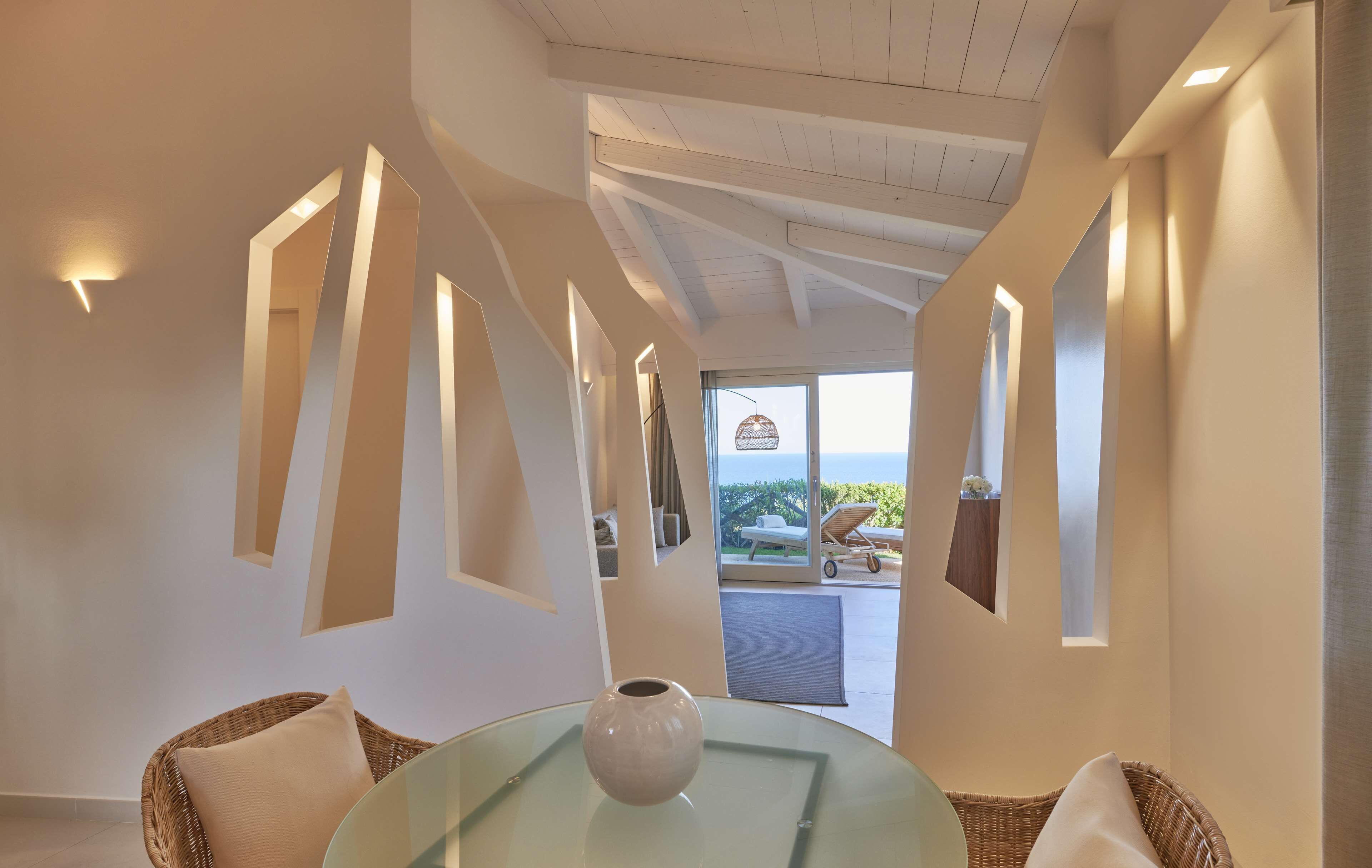 Un intérieur moderne avec une table en verre, des chaises en osier et une vue sur l’extérieur.