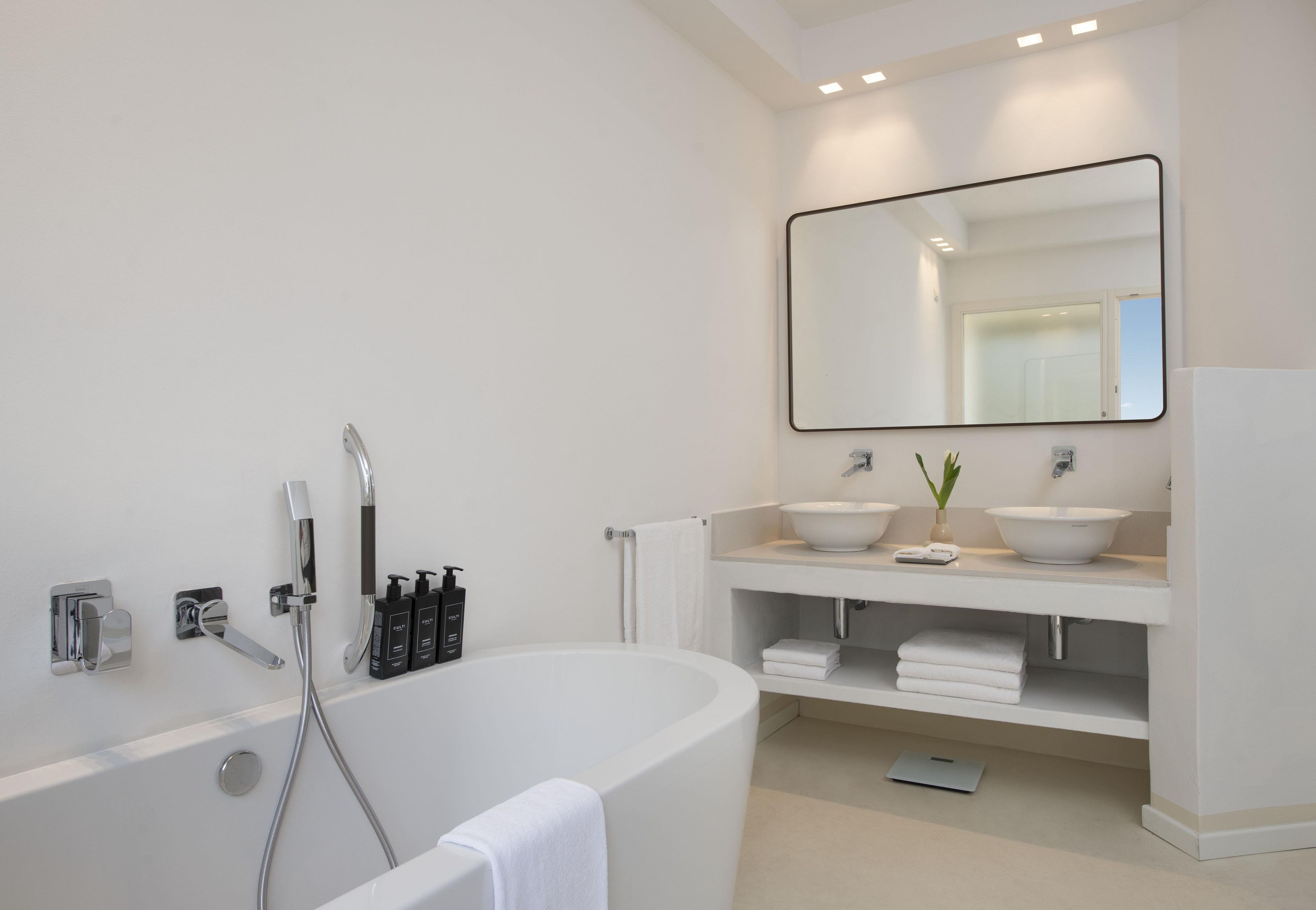 A modern bathroom with a freestanding bathtub, two sinks, a large mirror, and a towel rack.