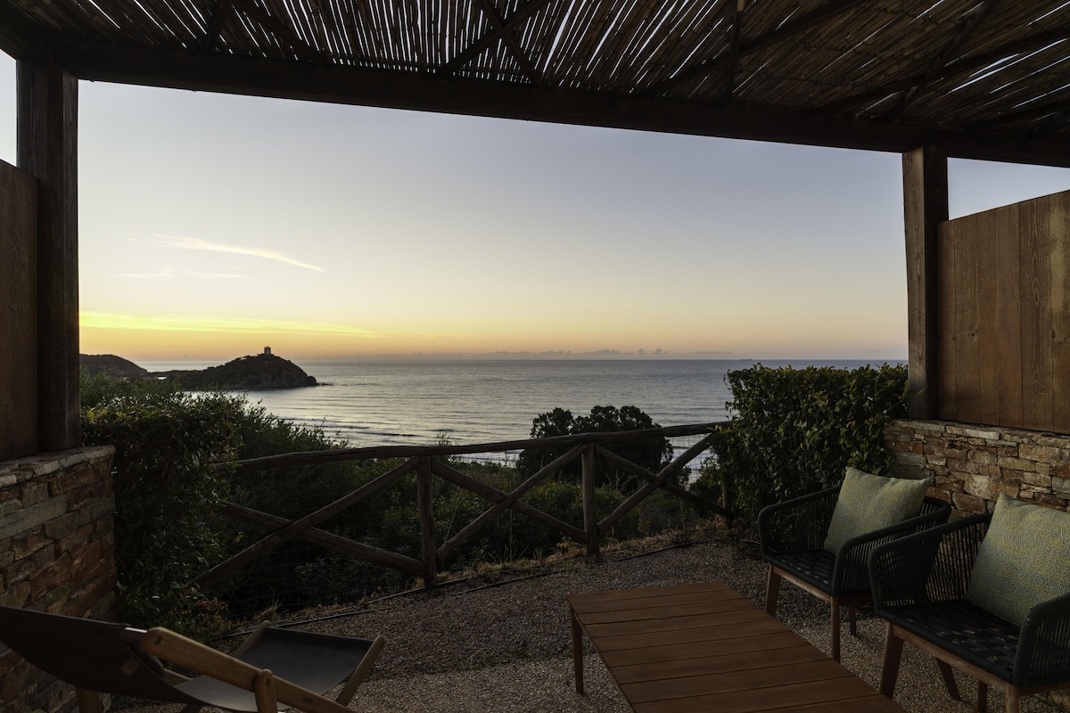 Una terraza de madera con vista al mar, un muro de piedra y una pérgola de madera.