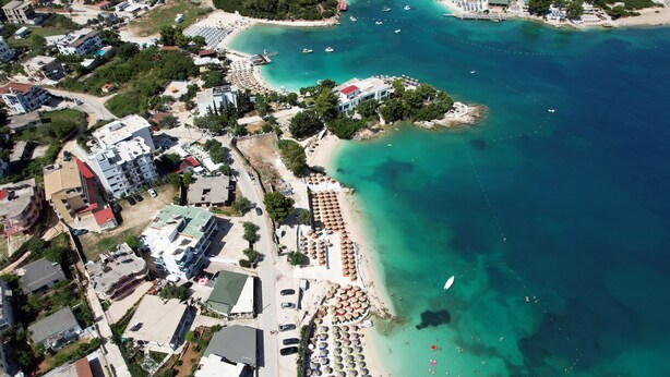 An aerial view of a coastal area with a beach, buildings, and boats. - Esmerald Hotel (Ksamil)