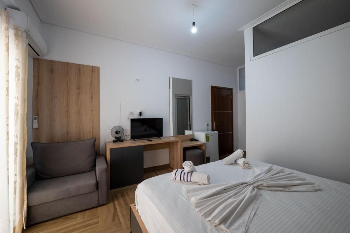 Quarto de hotel com cama, escrivaninha, televisão, guarda-roupa e sofá.